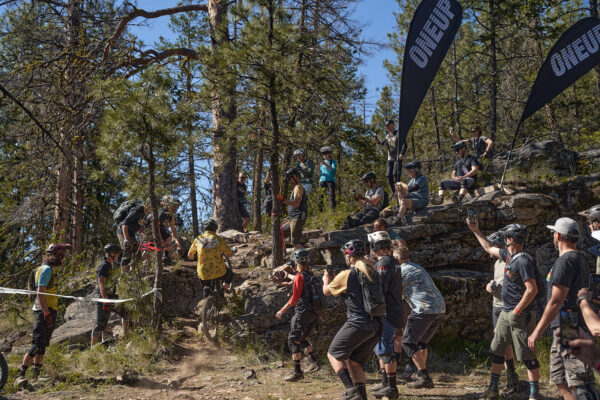 mountain biker climbing up a technical trail feature with a crowd cheering him on