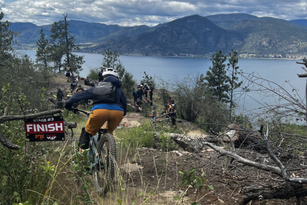 mountain biker crossing a singletrack finish line with lake and mountain view in the background