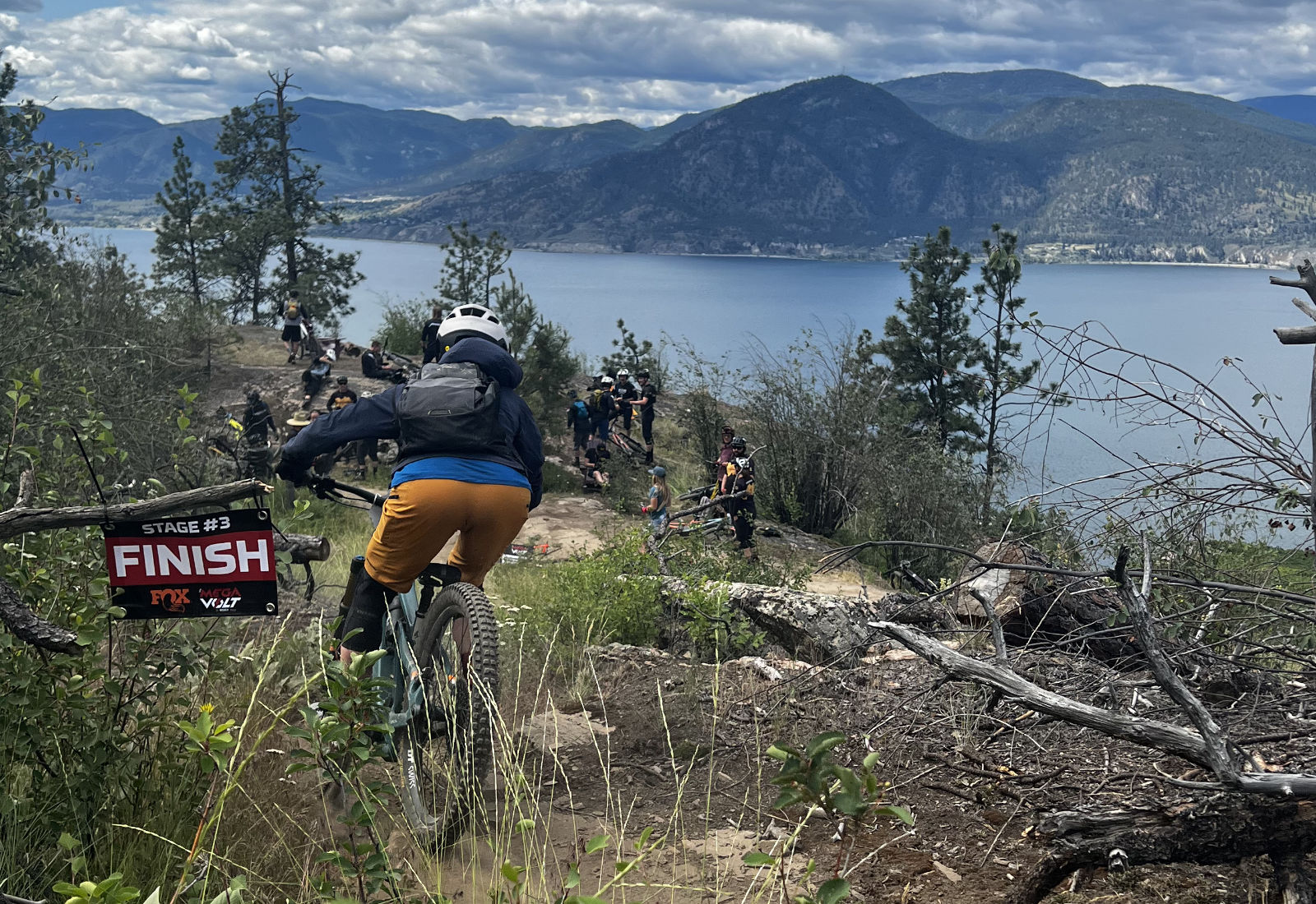 mountain biker crossing a singletrack finish line with lake and mountain view in the background