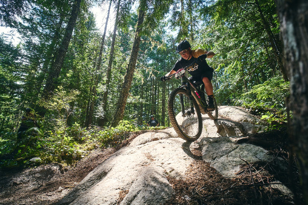 mountain biker on a rock roll, surrounded by evergreen trees with the sun shining through